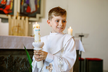 Little kid boy receiving his first holy communion. Happy child holding Christening candle....