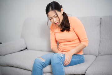 Obraz premium Young Asian beautiful woman leg while sitting on sofa at home, physical pain and therapist concept.