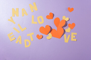 Letters and hearts cut from paper are randomly arranged on a pastel purple background. Space for decorations with the theme of anniversaries, Valentine's Day and more.
