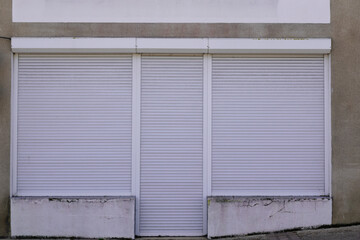 Fototapeta na wymiar closed store facade with white rolling shutter shop wall entrance