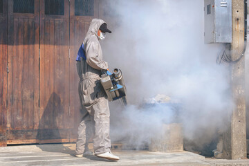 Healthcare worker using Fogging Machine Spraying chemical to eliminate Mosquitoes and prevent Dengue fever in drainage ditch along fence wall of house