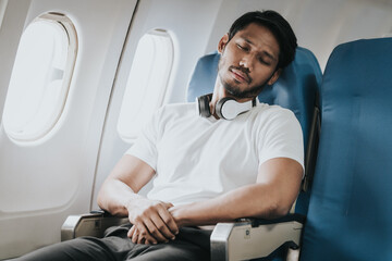 Asian male traveler on an airplane, appearing to have a headache or discomfort, showing a moment of...