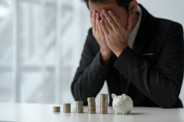 Businessman covers his face with his hands against a stack of coins, perspective on planning...