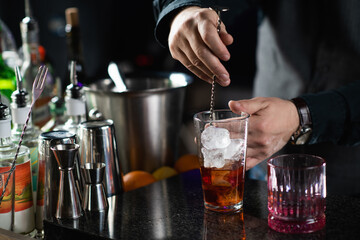 Fototapeta na wymiar Bartender mixing Negroni cocktail with long stirring metal spoon
