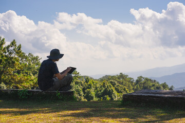 landscape and travel concept with solo freelancer man sit on wooden and use tablet work from outdoor with layer of mountain background