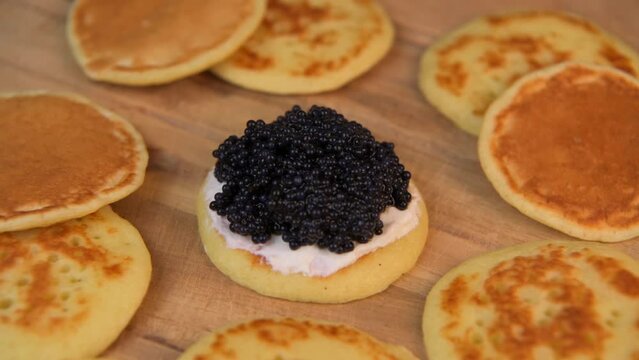 Blinis with black caviar and cream cheese, on a festive dish, mini pancakes, an elegant appetizer, High quality 4k footage