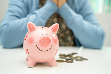 Asian elderly woman putting coin into pink piggy bank for saving money and insurance, poverty,...
