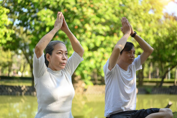 Older active couple doing breathing exercise in the summer park. Healthcare and meditation concept.