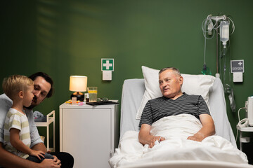 The older man, amidst his hospital stay, finds solace in the visit from his son and grandson, their...