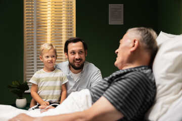 A grandson visits his grandfather in the hospital. The elderly man is lying in a hospital bed and...