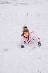 Fototapeta na wymiar Little smiling girl lying on her stomach in the snow