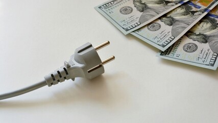 Electrical plug with cable and dollar bills on a white background. Electricity bill saving concept. The concept of attracting money energy.