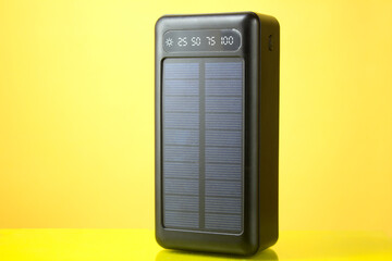 Portable solar-powered charger for a smartphone on a yellow background, close-up.