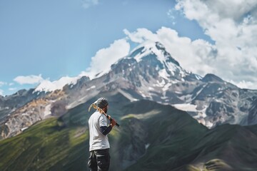 Amidst the Silence of the Alps. A Hiker’s Pause Amidst Majestic Peaks with Snow-Capped Mountains and a Clear Sky as Backdrop. Hiker with pickaxe view from the rear.