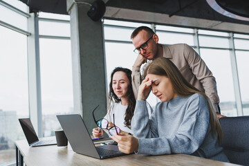 Young business woman typing on a keyboard, researching digital designs for a new advertising project, sitting in a chic office. Headache from working in the office