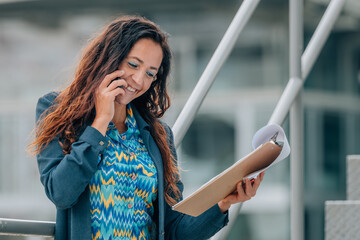 business woman talking on mobile phone on the street with documents © carballo