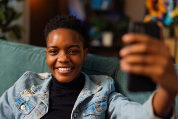 Portrait of delighted afo american dark skinned woman blogger vlogger taking selfie photo on camera...