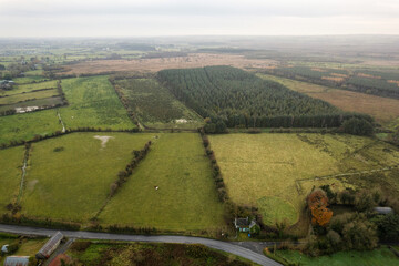 Aerial view on Irish country side with green grass farmland and patches of bushes and forest, blue cloudy sky. West of Ireland. Rural agriculture area scene.