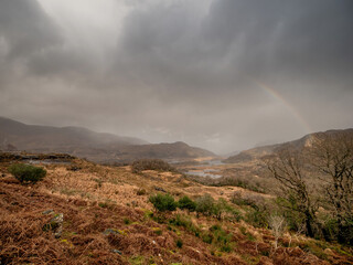 Rainbow over magnificent nature scene with valley in a mountains and dark dramatic sky. Ladies view, Killarney, Ireland, ring of Kerry route. Magnificent Irish nature and popular tourist area.