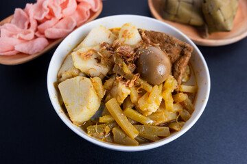 Ketupat Sayur or Lontong Sayur, a typical Indonesian food. Served with pumpkin vegetables, boiled eggs and tofu stew and crackers. Served during Ramadan, Eid al-Fitr and Adha. Black Background