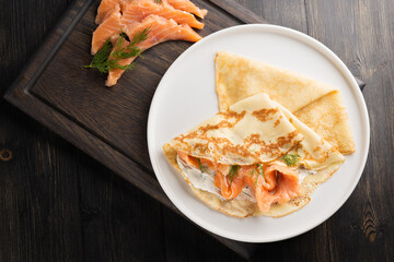 pancakes with salted salmon, herbs and cottage cheese in close-up. Traditional Russian pancakes...