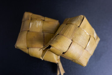 Ketupat still wrapped in coconut leaves isolated on a black background