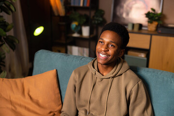 African man sitting comfortably on couch in a bright and spacious living room decorated with modern...