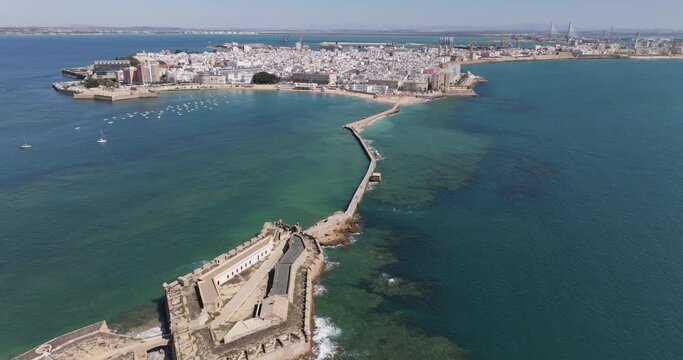 Aerial drone cityscape view of Cádiz in Spain, Andalusia, Europe, on bright sunny day, facing La Caleta beach and city waterfront. Drone slowly flying backwards. Shot in 5K ProRes 422 HQ