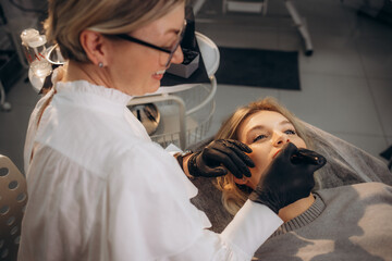Cosmetologist makes permanent makeup on a woman's face. Specialist applies a tattoo on the...