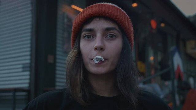 Close up portrait of a hipster girl in the city on the street, blowing bubble gum. A fashionable woman of generation Z. A female millennial chews chewing gum in town. Slow motion