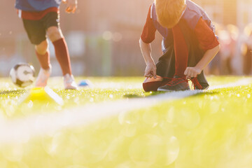 Young boy tie soccer shoe cleats on grass pitch during training. Children on sports football...