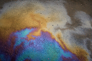 Fototapeta na wymiar Multi-colored poisonous spots of spilled gasoline on wet pavement during rain.