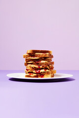 High Stack of Peanut Butter and Jelly Sandwiches on Plate with Purple Background