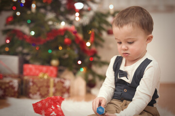 Little boy at time of christmas day unpacking gifts near tree