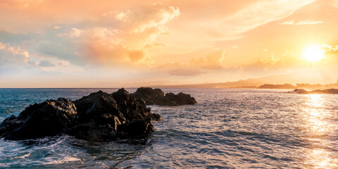 beautiful coast beach with sea gulf water during sunset or sunrise with golden sand, nice black rocks and stones, colorful vawes and clouds in thr sky