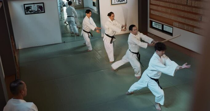 People, sensei and practice with weapon in dojo for fighting, training or karate class. Martial arts group with trainer or master in stancing for etiquette, attitude or commitment with black belt