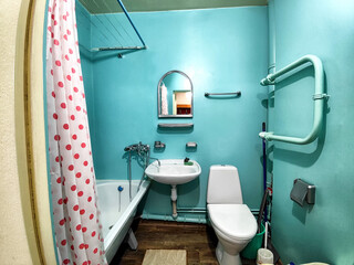 The interior of a small, modest bathroom with a bath and a toilet. Green walls, curtains with a red...