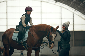 Female instructor teaching little girl, child horseback rising. Kid practicing trail riding,...