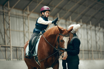 Good lesson,. Little girl giving high five to her instructor. Learning horseback riding on special...