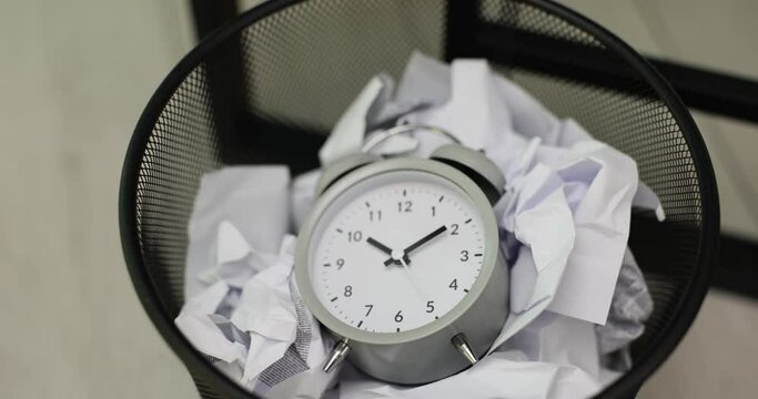 Alarm clock and woman hand throws it into trash can made of crumpled paper