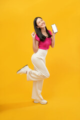 full-body portrait of an happy Asian woman holding a cell phone on a yellow background