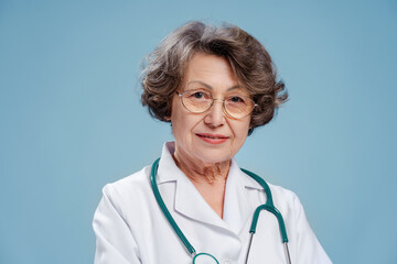 Portrait of smiling 70 year old woman, doctor wearing white coat, stethoscope, looking at camera