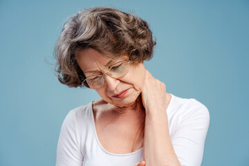 Portrait of upset gray haired senior woman wearing eyeglasses, having neck pain with closed eyes