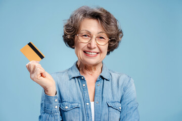 Beautiful 70 year old smiling woman holding credit card wearing eyeglasses looking at camera