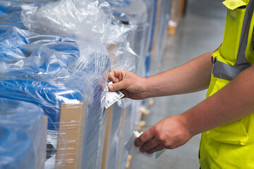 un ouvrier manutentionnaire qui colle une étiquette sur une cargaison sur palette - obrazy, fototapety, plakaty