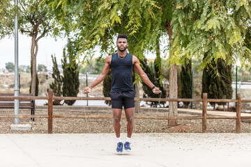 Fototapeta premium Strong sportsman jumping rope against green trees