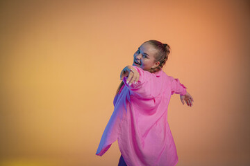 A young woman in a pink shirt poses against an orange studio background. The dancer demonstrates elements of jazz-funk choreography. Modern choreography.