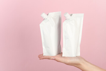 White doy packs with dispensers on hand palm, pink background. Template for design, mockup