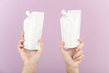 Hands holding white doy packs with dispensers on purple background. Template for design, mockup