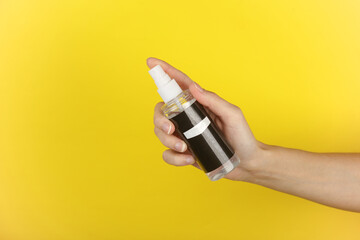 Hand holding a bottle of water protection shoe spray on a yellow background
